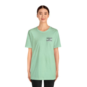 Woman wearing a light green unisex jersey t-shirt with "EXPERIENCE OVER EXTRAVAGANCE" text.