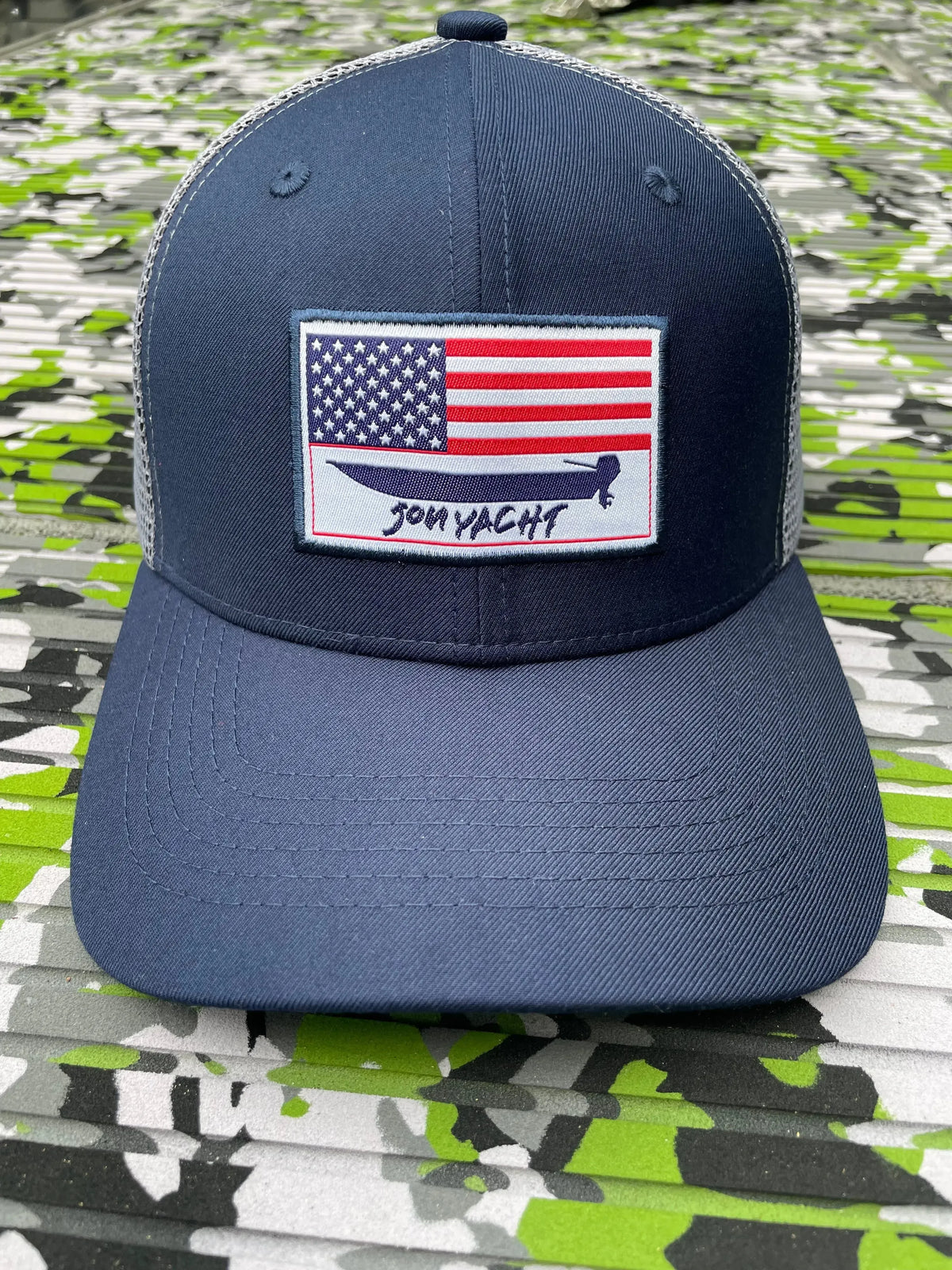Navy blue trucker hat with an embroidered American flag and "Jon Yacht" logo.