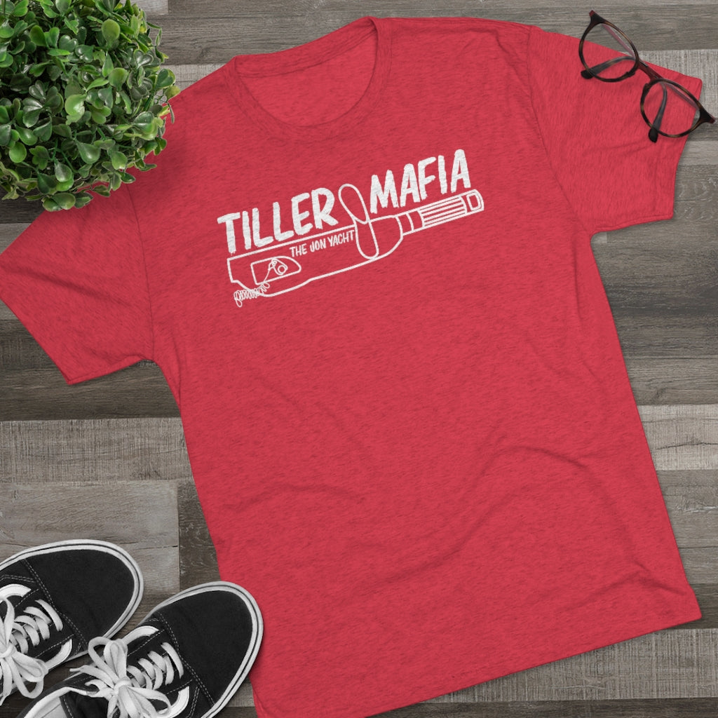 Red tri-blend "Tiller Mafia The Iron Yacht" graphic tee, black sneakers, and glasses on wood.