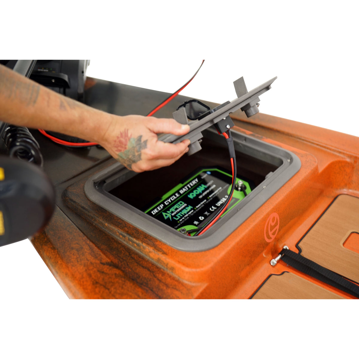 Hand installing a green deep cycle lithium battery into an orange Crescent Cres-Craft fishing skiff.
