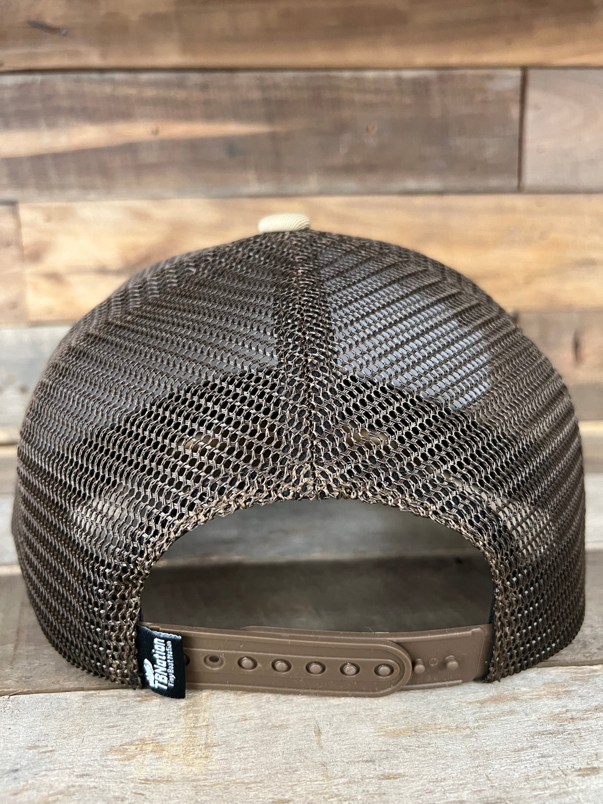 Back of a brown mesh trucker hat with a snapback closure and a small black "Tiny Boat Nation" tag.