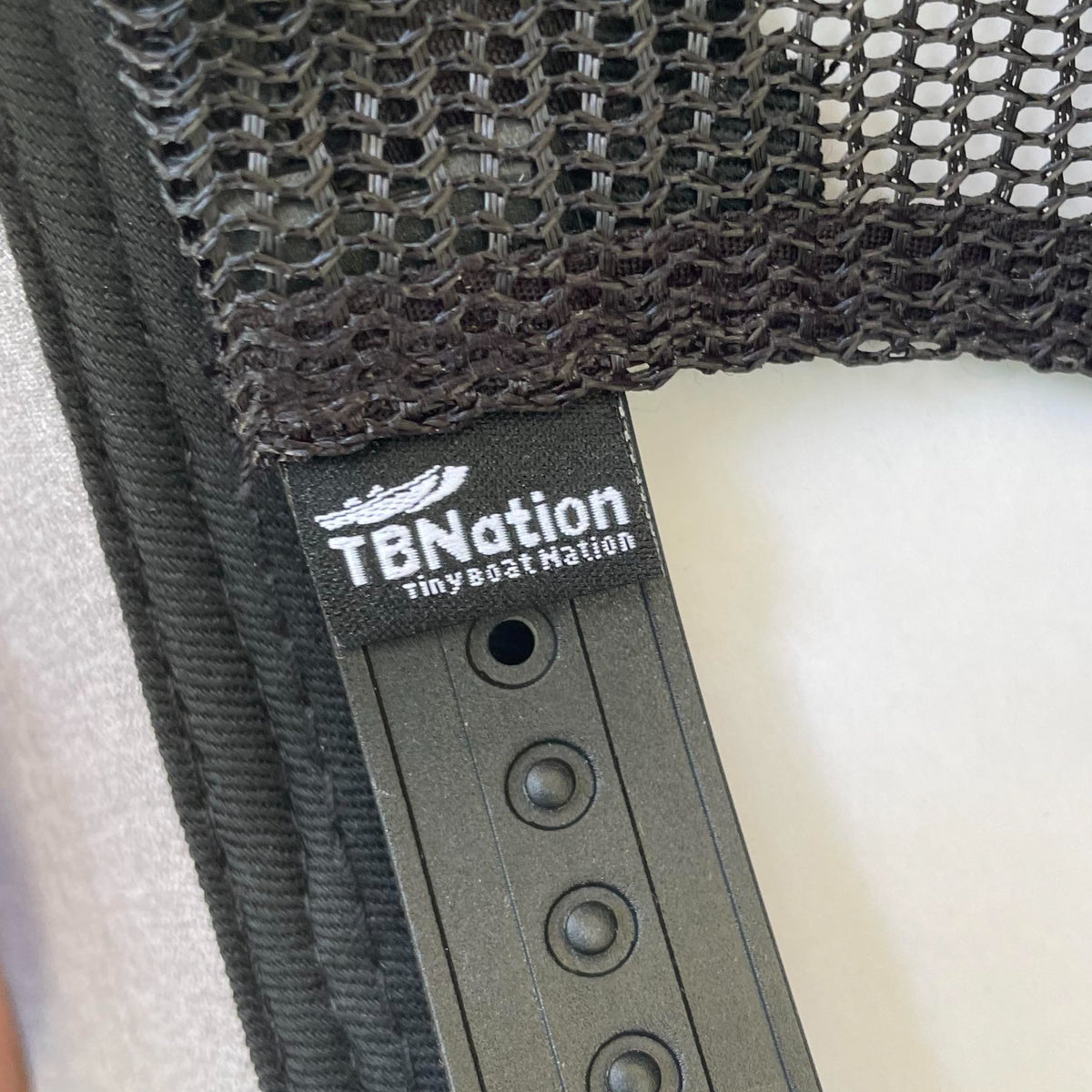 Black mesh trucker hat with a "TBNation Tiny Boat Nation" tag and adjustable snapback closure.