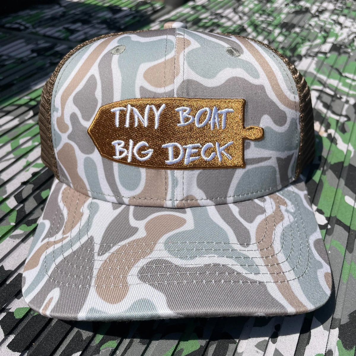 Camo "Tiny Boat Big Deck" hat with brown mesh back and embroidered boat patch.