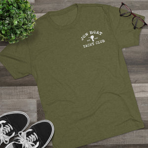 Olive green tri-blend tee with "Jon Boat Yacht Club" logo, black sneakers, plant, and glasses on wood.