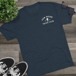 Navy tri-blend tee with "Jon Boat Yacht Club" logo, black sneakers, plant, and glasses on wood.