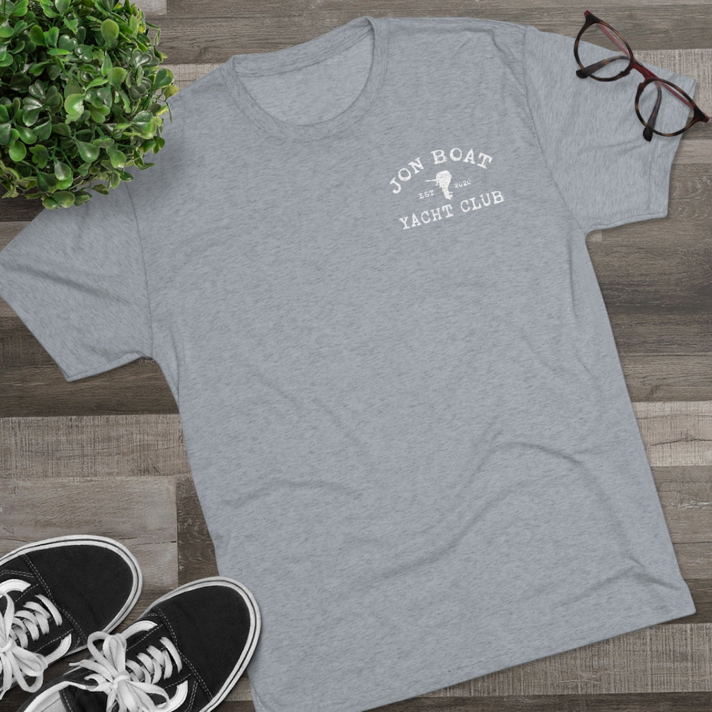 Light gray tri-blend t-shirt with "Jon Boat Yacht Club" logo, black sneakers, plant, and glasses on wood.