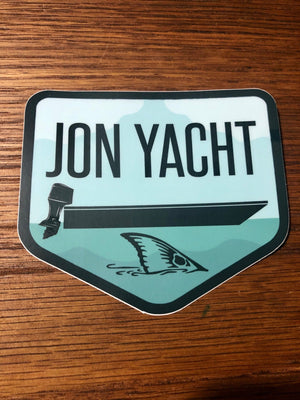 Jon Yacht Tailer 4" sticker with a black boat, motor, and shark fin on a light blue water background.