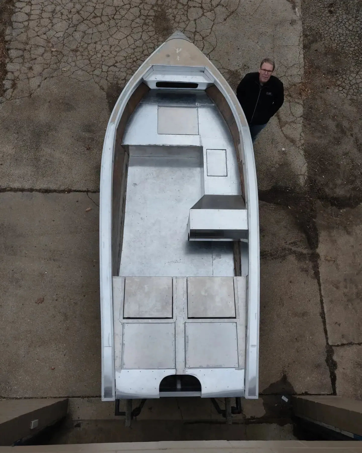 Overhead view of a silver aluminum boat with a man standing beside it, showcasing the DIY drop-in stowable seat design.