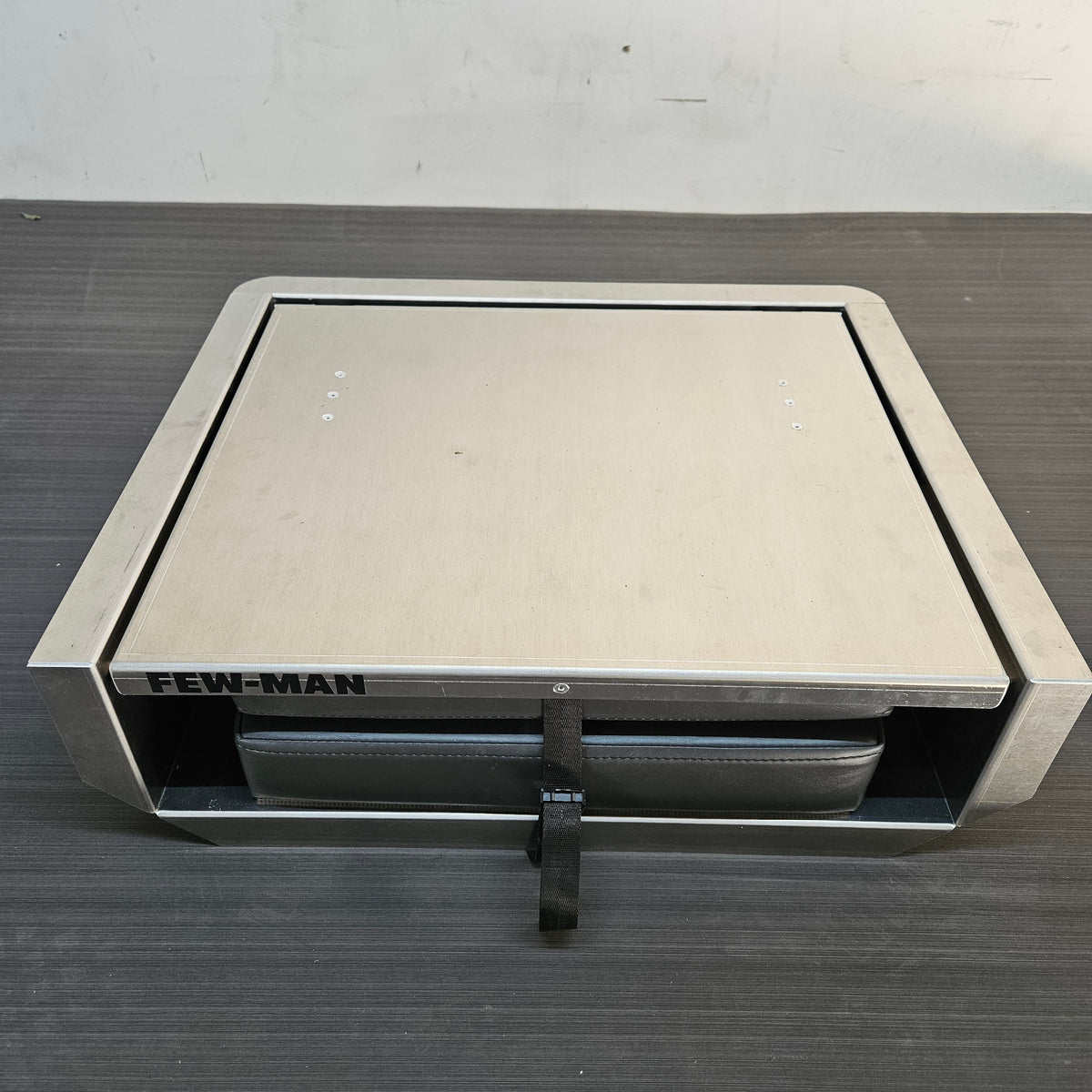 Silver aluminum Few-Man JumpSeat with a charcoal vinyl cushion and black cinch strap, designed for boat decks.