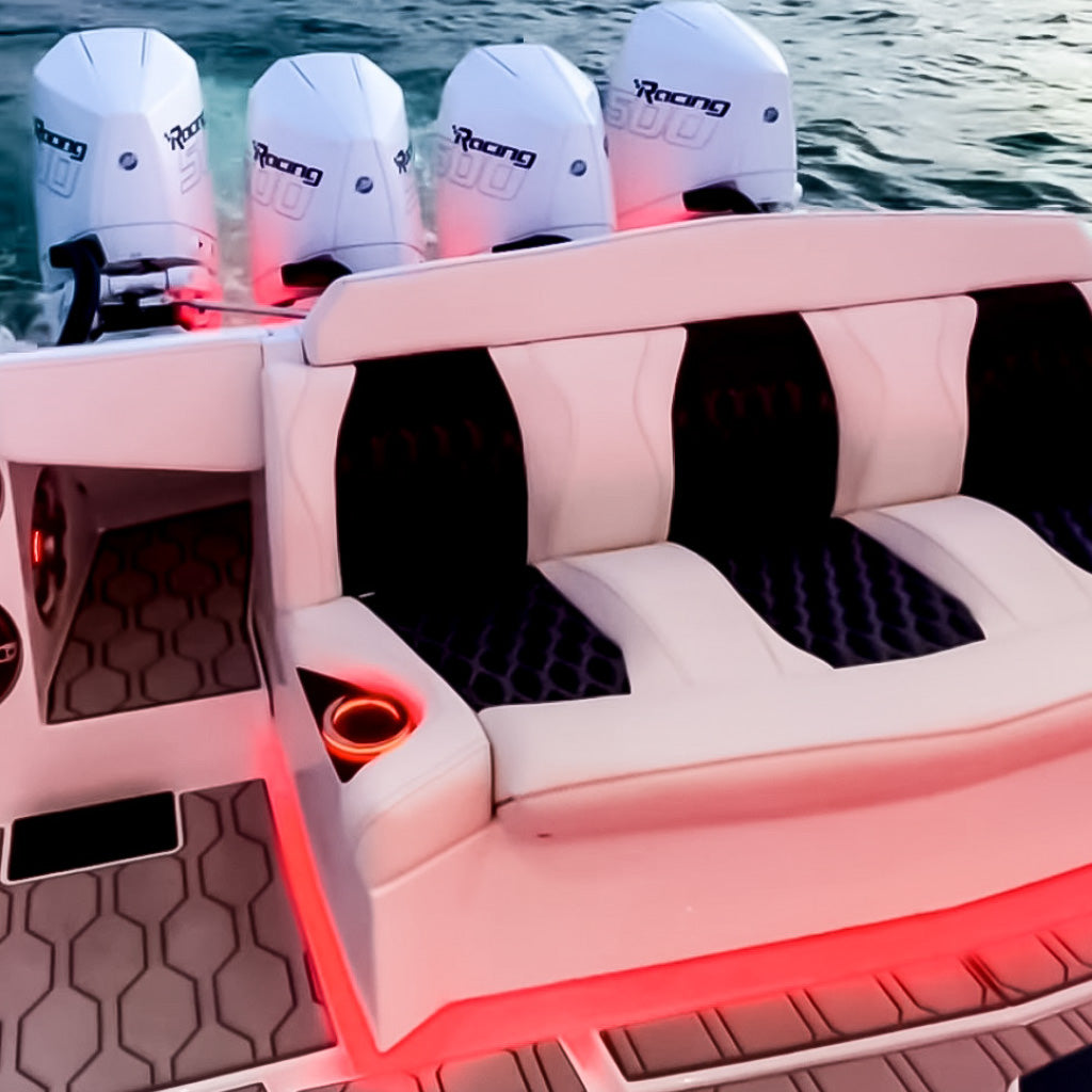 White boat with four outboard motors, featuring white and black upholstered seating, red ORBIT Neon Flex side-shooting lights, and a patterned deck.