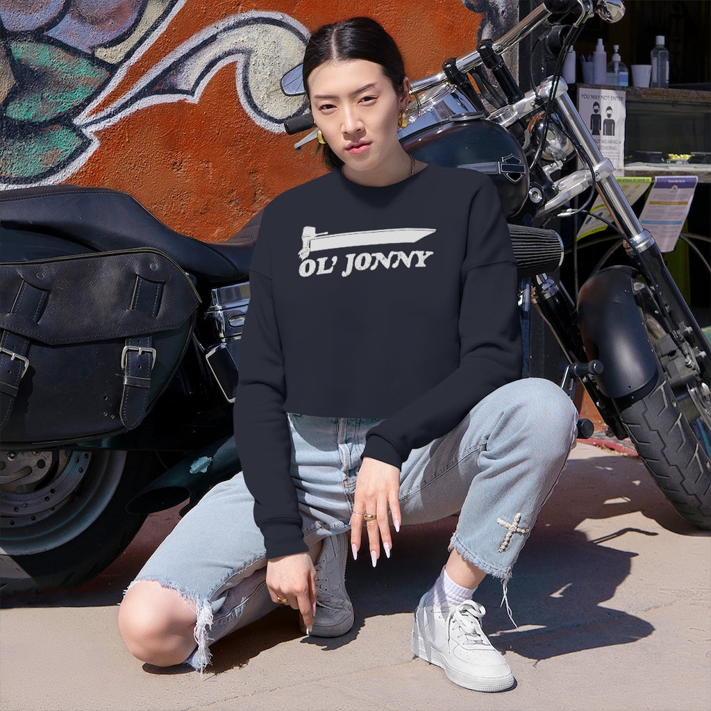 Woman in black Ol' Jonny cropped sweatshirt, light wash ripped jeans, and white sneakers by a motorcycle.