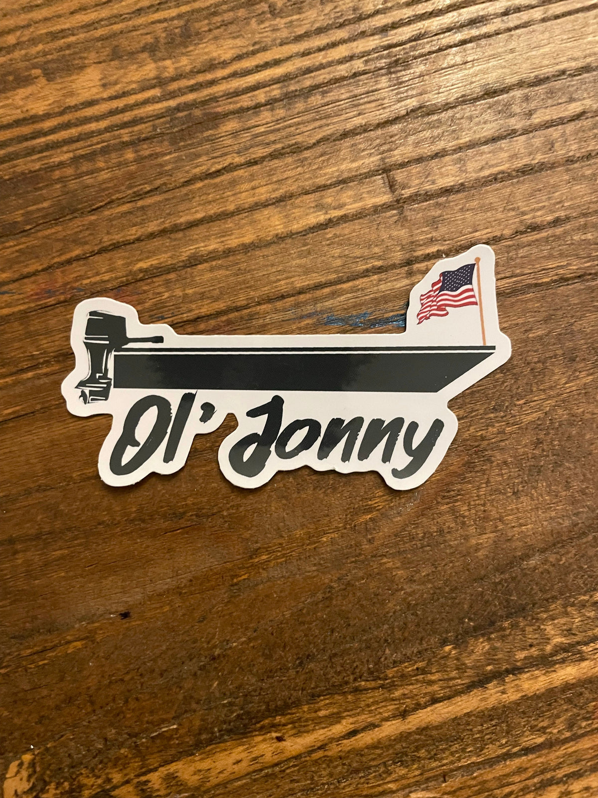 White die-cut Ol' Jonny sticker featuring a black boat with an outboard motor and an American flag.