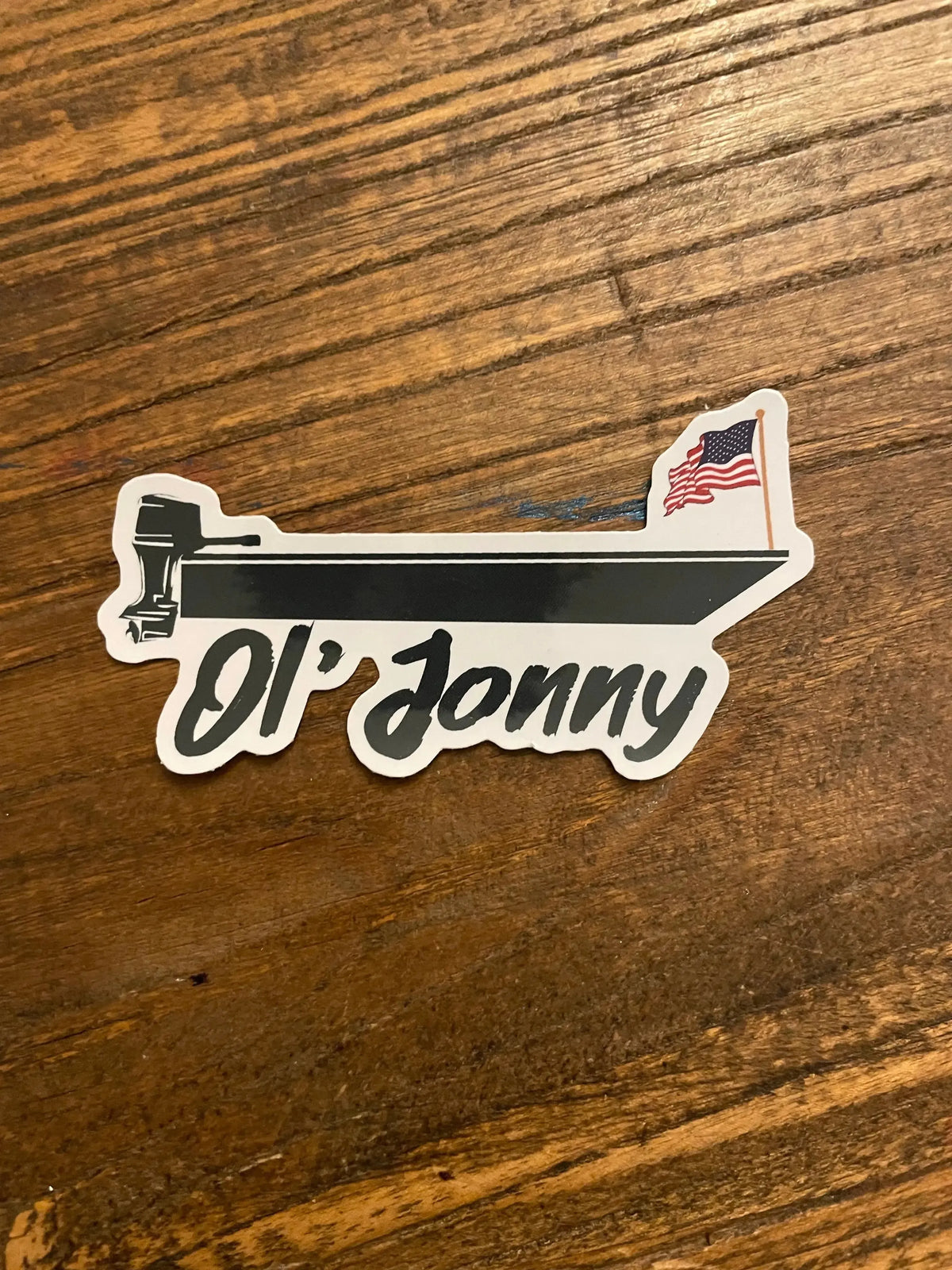 White die-cut Ol' Jonny sticker featuring a black boat with an outboard motor and an American flag.