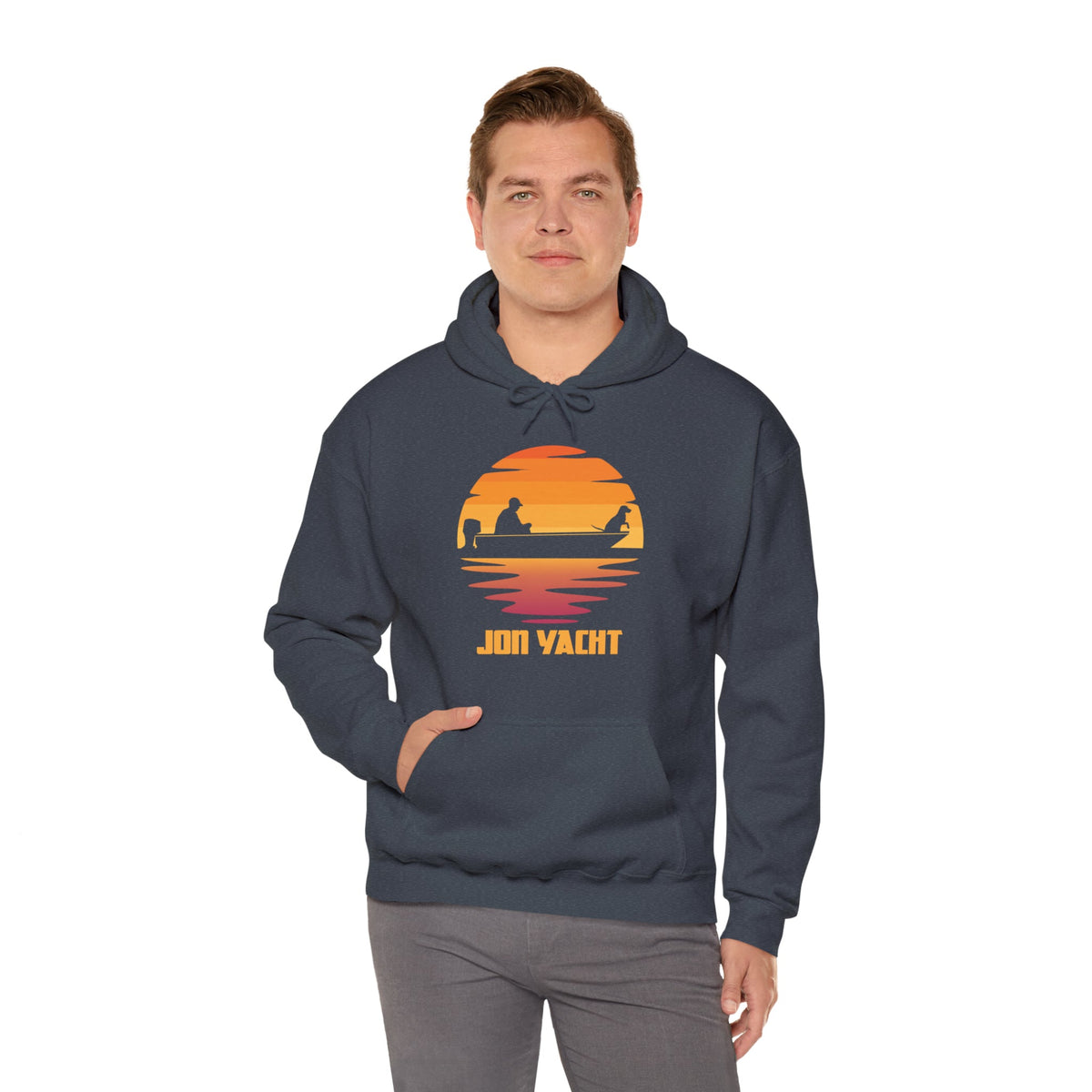 Man wearing a dark gray "Jon Yacht" hoodie with a sunset and boat graphic, hand in kangaroo pocket.