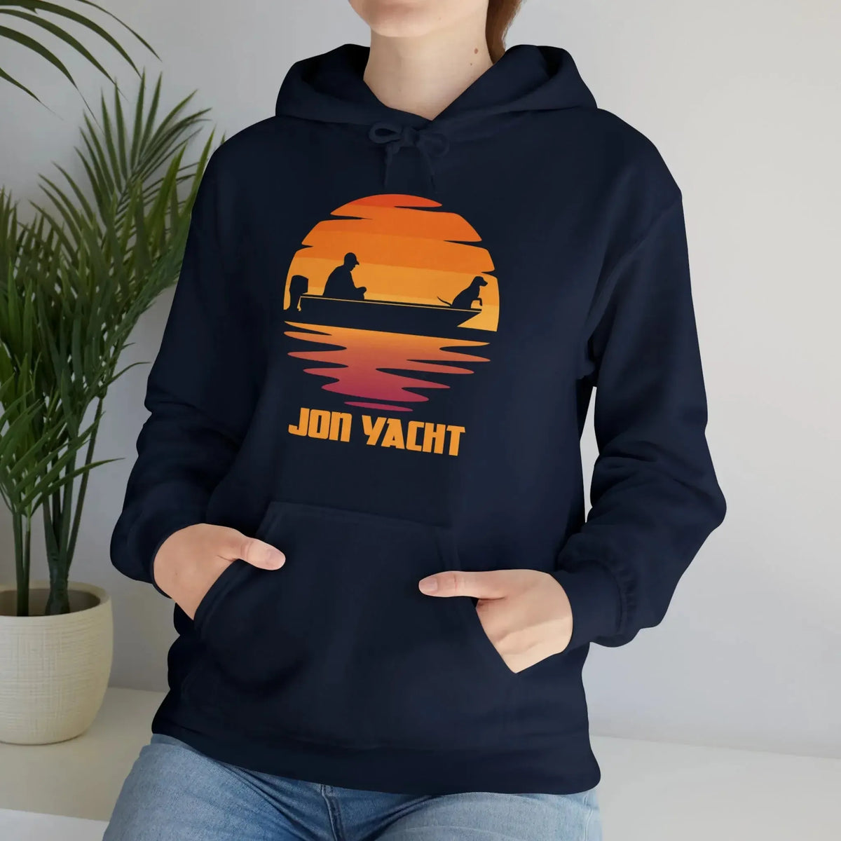 Navy blue hoodie with a sunset graphic featuring a person and dog in a boat, "JON YACHT" text, and a kangaroo pocket.