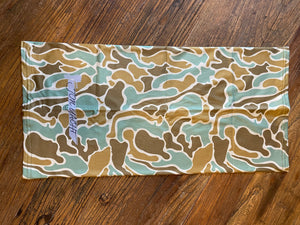 Old School Buff with light "Pluff Mud" camouflage pattern in greens, browns, and white, folded on wood.