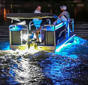 Pontoon boat at night with bright blue and yellow RGBW Plashlight strips illuminating the water.