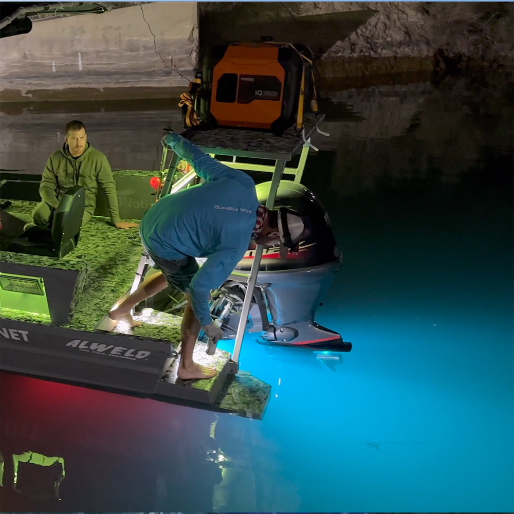 Man installing a Plashlights EPIK dual color underwater transom light on a boat, illuminating the water in bright blue.