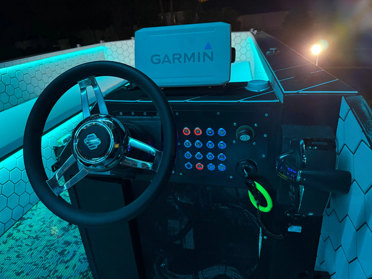 Boat dashboard with black steering wheel, Garmin display, and Plashlights REVERT 22mm switches with blue and red LED rings.