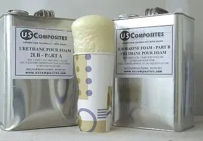 Expanding yellow urethane pour foam overflowing from a paper cup, flanked by two metal US Composites cans.