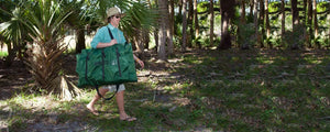 Man in a straw hat and green shirt carrying a packed Hunter Green Sea Eagle 285 frameless inflatable fishing boat.