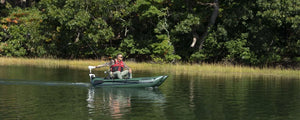 Man fishing from a Hunter Green Sea Eagle 285 Frameless Pontoon Boat with a trolling motor on a calm lake.