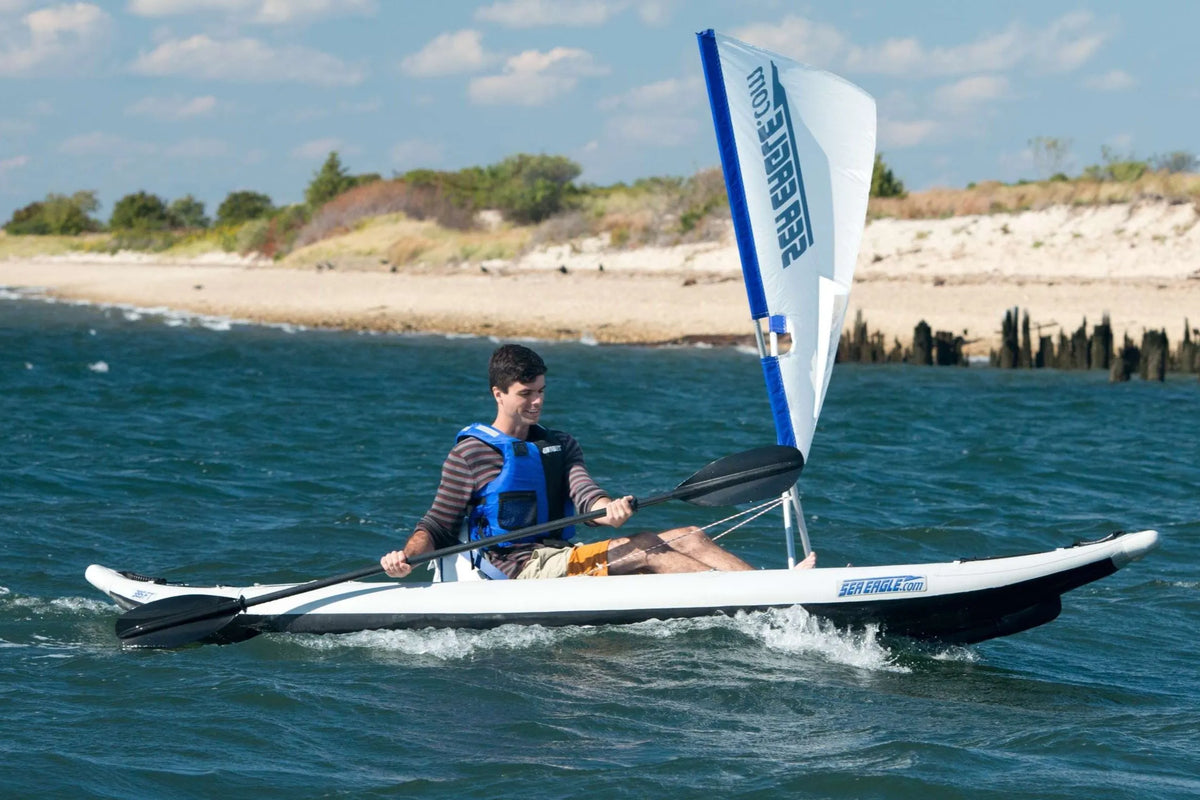 Man in a blue life vest paddling a white and black Sea Eagle FastTrack inflatable kayak with a sail.