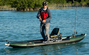 Man stands on a green and black Sea Eagle FastTrack Angler inflatable kayak with fishing rods.
