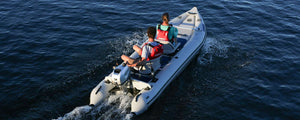 Two people in red life vests motor a white Sea Eagle 437ps PaddleSki inflatable catamaran on blue water.
