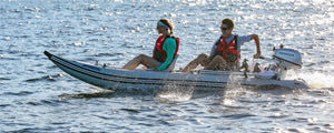 Two people in red life vests ride a gray Sea Eagle 437ps PaddleSki inflatable catamaran with a Honda motor.