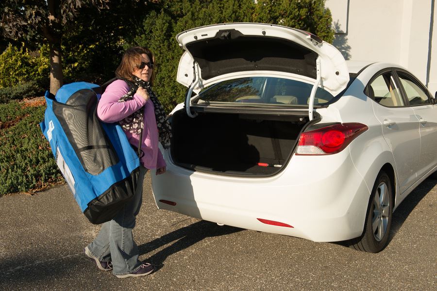 Woman carrying a large blue Sea Eagle backpack with mesh panels towards an open white car trunk.