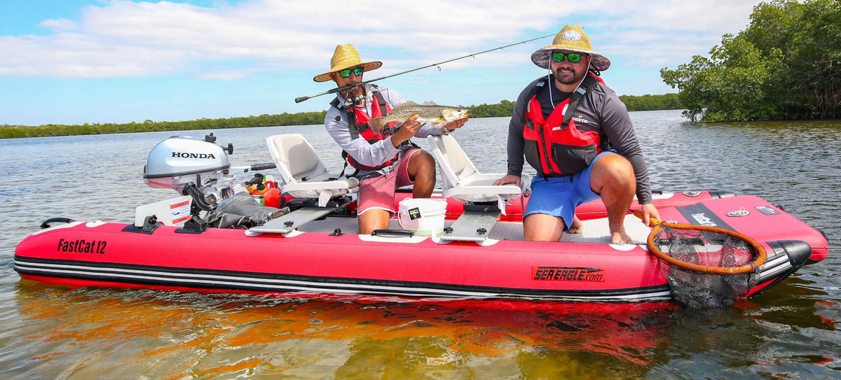 Two men fishing from a red Sea Eagle FastCat12 inflatable catamaran with a Honda outboard motor.