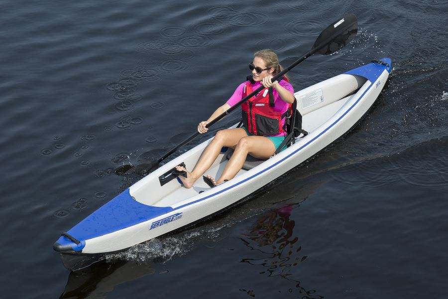 Woman paddling a white and blue Sea Eagle inflatable kayak with black FlexBrace adjustable footrests.