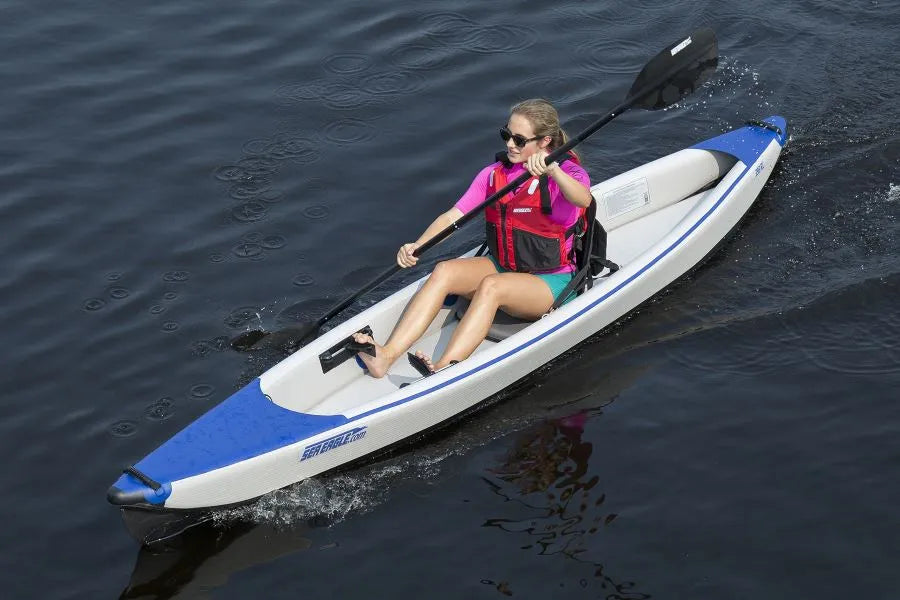 Woman kayaking in a white and blue inflatable kayak, using black Sea Eagle FlexBrace footrests.