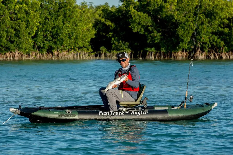 Man in a green inflatable kayak with a swivel seat fishing rig, holding a fish.