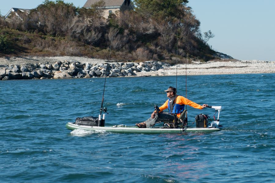 Man fishing from a green Sea Eagle iSUP with a swivel seat, two Scotty rod holders, and a trolling motor.
