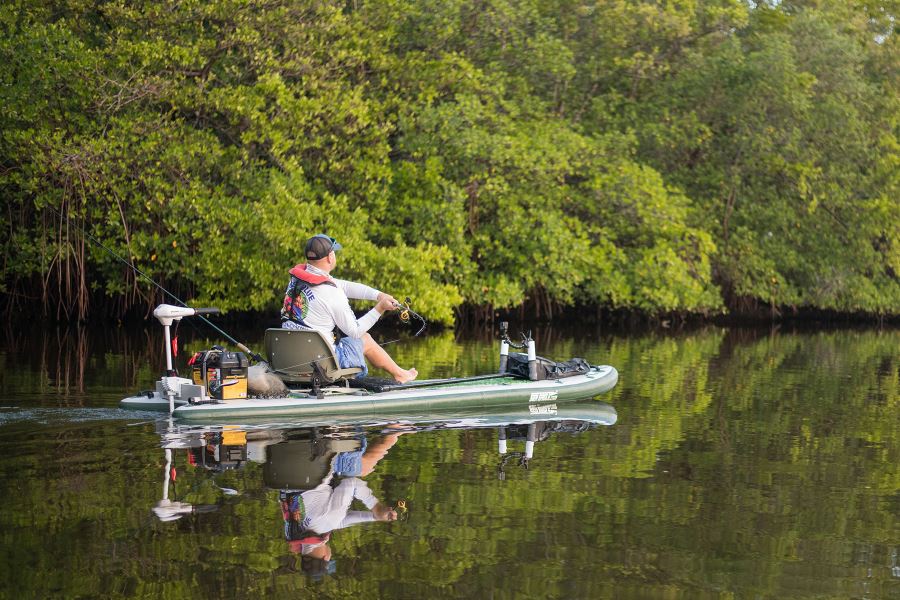 Green Sea Eagle iSUP with a swivel seat fishing rig, Scotty rod holders, and a man fishing.