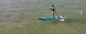 Man paddleboarding on a blue and yellow Sea Eagle LongBoard 11 inflatable SUP on calm water.