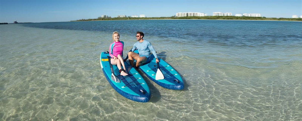 Two people on blue and teal Sea Eagle LongBoard 11 inflatable paddleboards in clear shallow water.