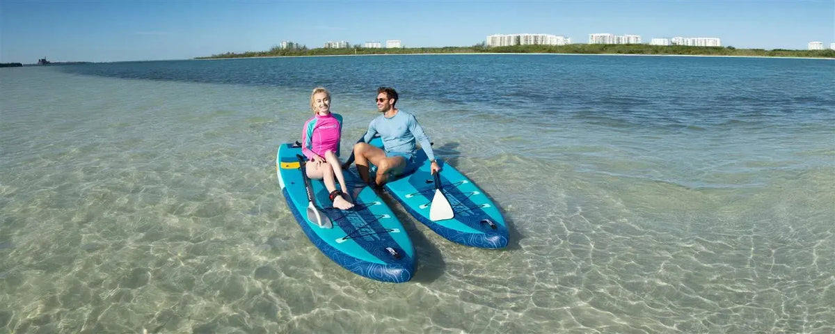 Two people on blue and teal Sea Eagle LongBoard 11 inflatable paddleboards in clear shallow water.