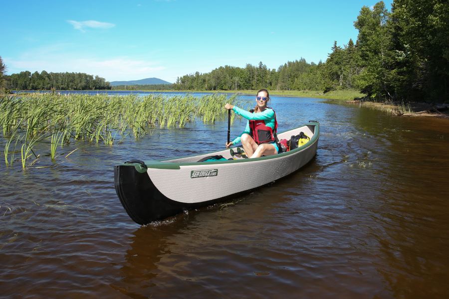 Woman paddling a Sea Eagle Travel Canoe with a wood/web seat on a sunny lake.