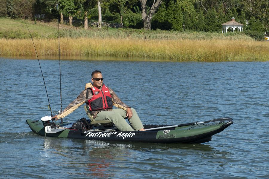 Man in a green and black FastTrack Angler kayak with a white electric motor mount, fishing rods, and a red life vest.