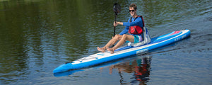Man paddling a blue and white Sea Eagle NeedleNose 14 inflatable SUP with a red life vest on calm water.