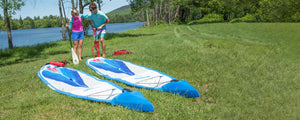 Two blue and white Sea Eagle NeedleNose™ 14 inflatable paddleboards on grass, with people nearby.