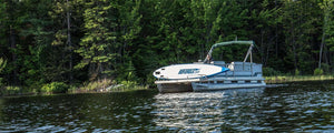 White and blue Sea Eagle NeedleNose 14 inflatable paddleboard on a pontoon boat, surrounded by a lake and trees.