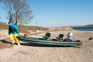 Man in blue hat and yellow pants pulling a green inflatable boat with a Sea Eagle EZ Cart on a sandy beach.