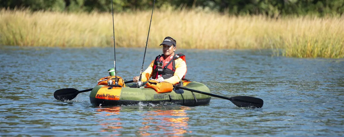 Green Sea Eagle PackFish7 inflatable fishing boat with an angler, oars, and fishing rods on calm water.
