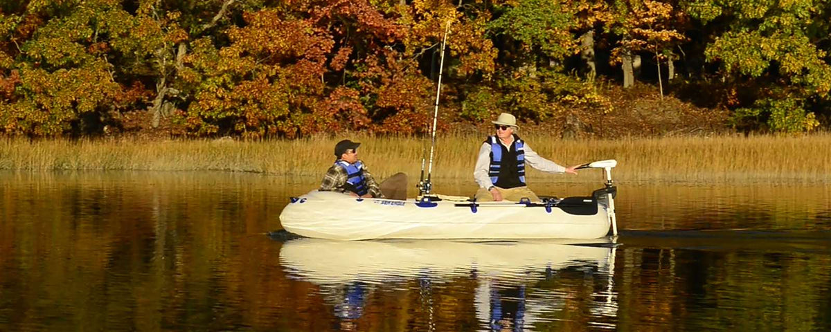 Two people fishing from a white Sea Eagle inflatable boat with an electric motor on a calm lake.