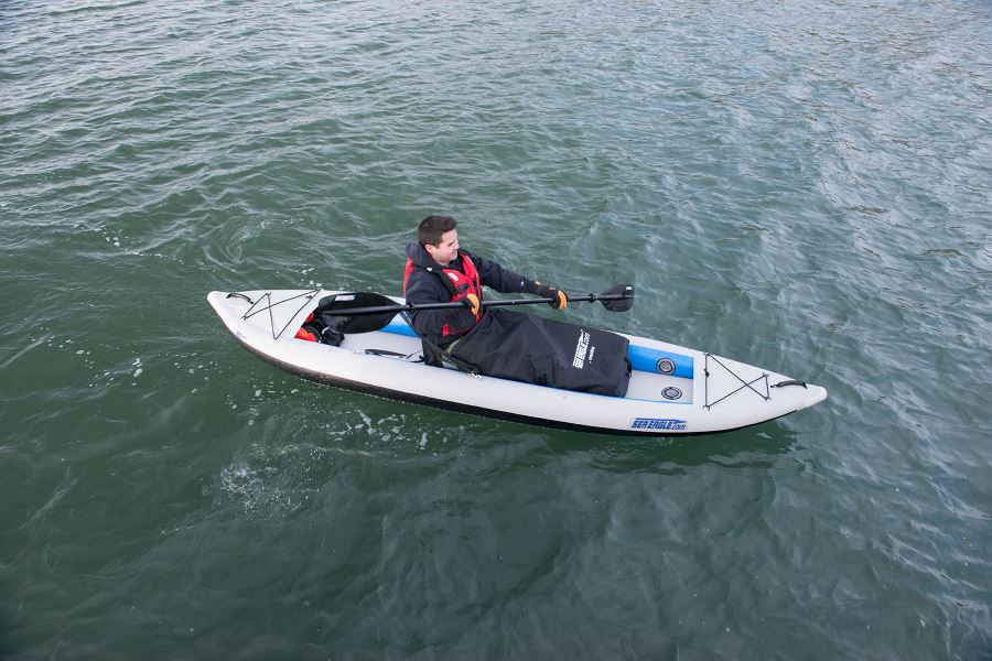 Person kayaking in a white Sea Eagle inflatable kayak with a black waterproof blanket covering their legs.