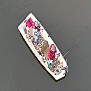Two anglers in a beige Sun Dolphin American 12 boat with camouflage flooring, fishing on calm water.